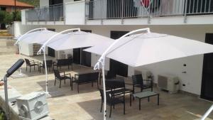 2 weiße Sonnenschirme auf einer Terrasse mit Stühlen und Tischen in der Unterkunft il Gelsomino in Formia
