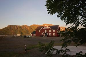 Une grande maison rouge avec des montagnes en arrière-plan dans l'établissement Toftenes Sjøhuscamping, à Alsvåg