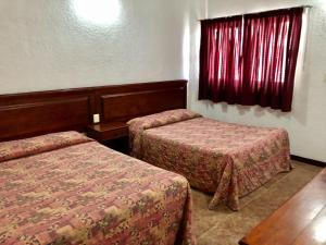 a room with two beds and a window with red curtains at Hotel Roma in Oaxaca City
