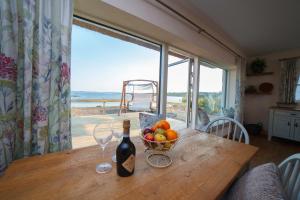 a table with a bowl of fruit and a bottle of wine at BaySide Cottage in Canower