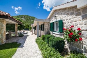 Duge Njive的住宿－Villa Silentio, complete privacy near Makarska，一座石头房子,设有绿色的窗户和红色的玫瑰