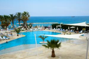 a large swimming pool with palm trees and the ocean at Venus Beach Hotel in Paphos