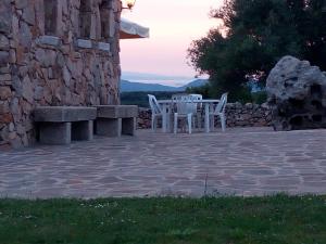 2 sillas blancas, mesa y pared de piedra en Turismo rurale l'Agliuledda, en Sant'Antonio di Gallura