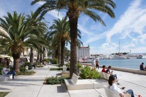 people sitting on benches next to the water with palm trees at Cvit Jadrana in Split
