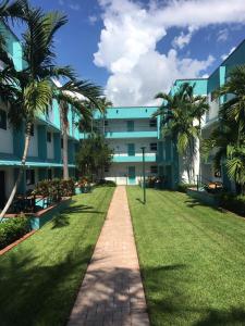 a walkway in front of a building with palm trees at Surf Rider Resort in Pompano Beach