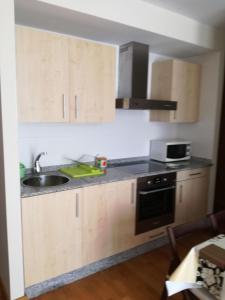 een keuken met houten kasten, een wastafel en een magnetron bij Apartamento Costa de Lugo in Foro