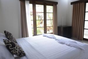 ein weißes Bett mit Kissen in einem Zimmer mit Fenstern in der Unterkunft Agung Trisna Bungalows in Ubud