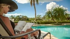 a woman sitting in a chair reading a book by a pool at Inn at Pelican Bay in Naples