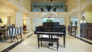 a piano in a living room with chairs and a table at Inn at Pelican Bay in Naples