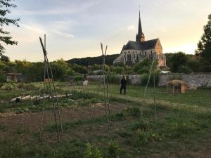 eine Person steht in einem Garten mit einer Kirche im Hintergrund in der Unterkunft Aux Delices de l'Abbaye in Orbais