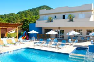 a pool with chairs and umbrellas in front of a building at Atena Praia Hotel in Boicucanga