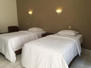 two beds in a hotel room with white sheets at Parama Hotel in Wonosobo