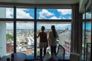 dos chicas de pie frente a una ventana en JR Kyushu Hotel Blossom Naha, en Naha