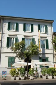 a white building with green shuttered windows and a tree at Hotel Ondina in Viareggio