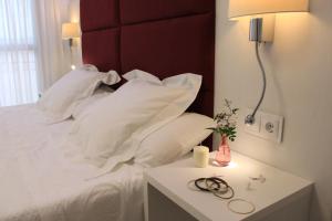 Cama con almohadas blancas y mesa con lámpara en Hotel Gran Proa Playa Raxó, en Raxó