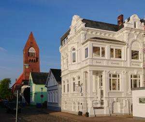 ein weißes Gebäude mit einer Kirche im Hintergrund in der Unterkunft Hotel Beckröge in Cuxhaven