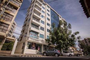 un grand bâtiment blanc avec des voitures garées devant lui dans l'établissement Apartamento Familiar Ideal, à Cochabamba