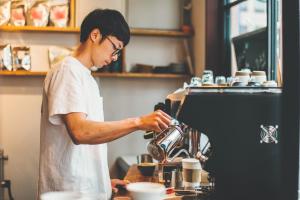 a man standing in a kitchen using a coffee machine at CITAN Hostel in Tokyo