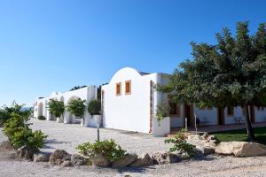 a row of white buildings with trees and rocks at Tenute Plaia Agriturismo in Scopello