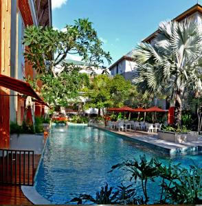 a swimming pool with tables and umbrellas next to a building at HARRIS Hotel & Residences Sunset Road in Kuta