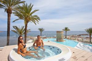 a man and a woman sitting on a beach next to a pool at Hotel Torre del Mar - Ibiza in Playa d'en Bossa