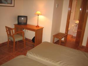 a room with a bed and a desk with a television at Hotel Chané in Puebla de Alfindén