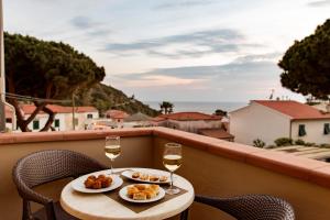 a table with two glasses of wine and food on a balcony at Hotel Corallo in Pomonte
