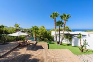 a patio with a bench and palm trees and the ocean at Villa Can Azul in Cala Tarida