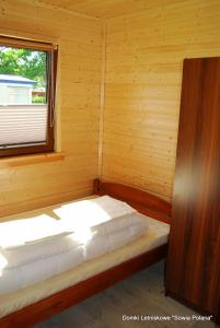 Łóżko w drewnianym pokoju z oknem w obiekcie Domki Sowia Polana w mieście Dąbki