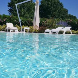 eine Gruppe weißer Stühle und ein Sonnenschirm in einem Pool in der Unterkunft Villa Onofria in Sirmione