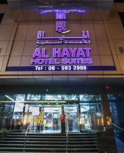 a man standing in front of a building with a neon sign at Al Hayat Hotel Suites in Sharjah