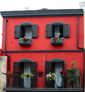 een rood gebouw met zwarte ramen en bloempotten bij Sa domu rubia in Iglesias