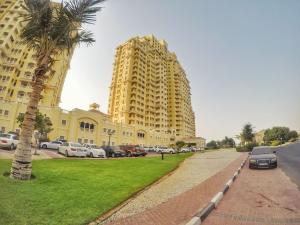 a large yellow building with cars parked in a parking lot at Haven Studio Apartments in Ras al Khaimah