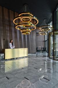 a woman standing at a counter in a lobby with chandeliers at Mennica Residence in Warsaw
