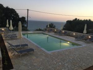 a swimming pool with chairs and umbrellas and the ocean at Anna Studios in Lourdhata