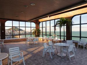 a restaurant with tables and white chairs and windows at Flat Pasárgada 712, pé na praia in Vila Velha