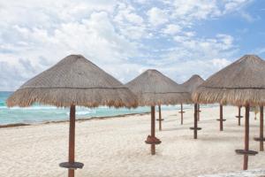 a row of straw umbrellas on a beach at Rodero by Solymar Beach Front Condos in Hotel Zone in Cancún