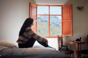 a woman sitting on a bed looking out of a window at Casona Plaza Ecolodge Colca in Yanque