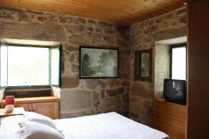a bedroom with a stone wall with a bed and a tv at A Casiña de Pedra in Noalla
