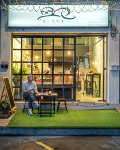 un hombre sentado en una mesa frente a una tienda en Sloth Hostel Don Mueang en Ban Don Muang (1)