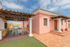 ein rosafarbenes Haus mit einer Terrasse mit einem Tisch und Stühlen in der Unterkunft Villa Bella Lucia 1. Piscina Climatizada, WiFi, BBQ. in Corralejo