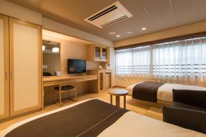 a bedroom with two beds and a desk with a television at Hana Beppu in Beppu