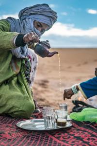 Una donna che versa acqua in un bicchiere su un tavolo di Desert Tours & Camp Chraika a M'Hamid