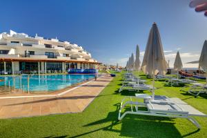 a pool with chairs and umbrellas next to a large building at SBH Crystal Beach Hotel & Suites - Adults Only in Costa Calma