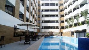 una piscina al aire libre con mesas y sillas y un edificio en Littoral Gold Flat, en João Pessoa