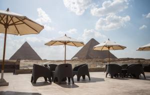 a patio with chairs and umbrellas and the pyramids at Hayat Pyramids View Hotel in Cairo