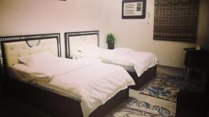 two beds in a bedroom with white sheets at Almalki furnished units in Al Thybiyah