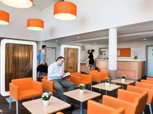 a man sitting in a restaurant with orange chairs at ibis budget Brugge Centrum Station in Bruges