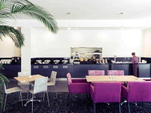 a restaurant with tables and purple chairs and a chef in the kitchen at Mercure Newcastle Airport in Newcastle