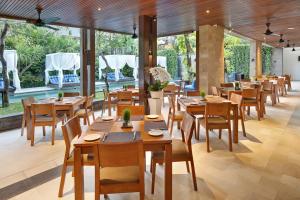 スミニャックにあるザ エリシアン ブティック ヴィラ ホテルの木製のテーブルと椅子、大きな窓のあるレストランを併設しています。
